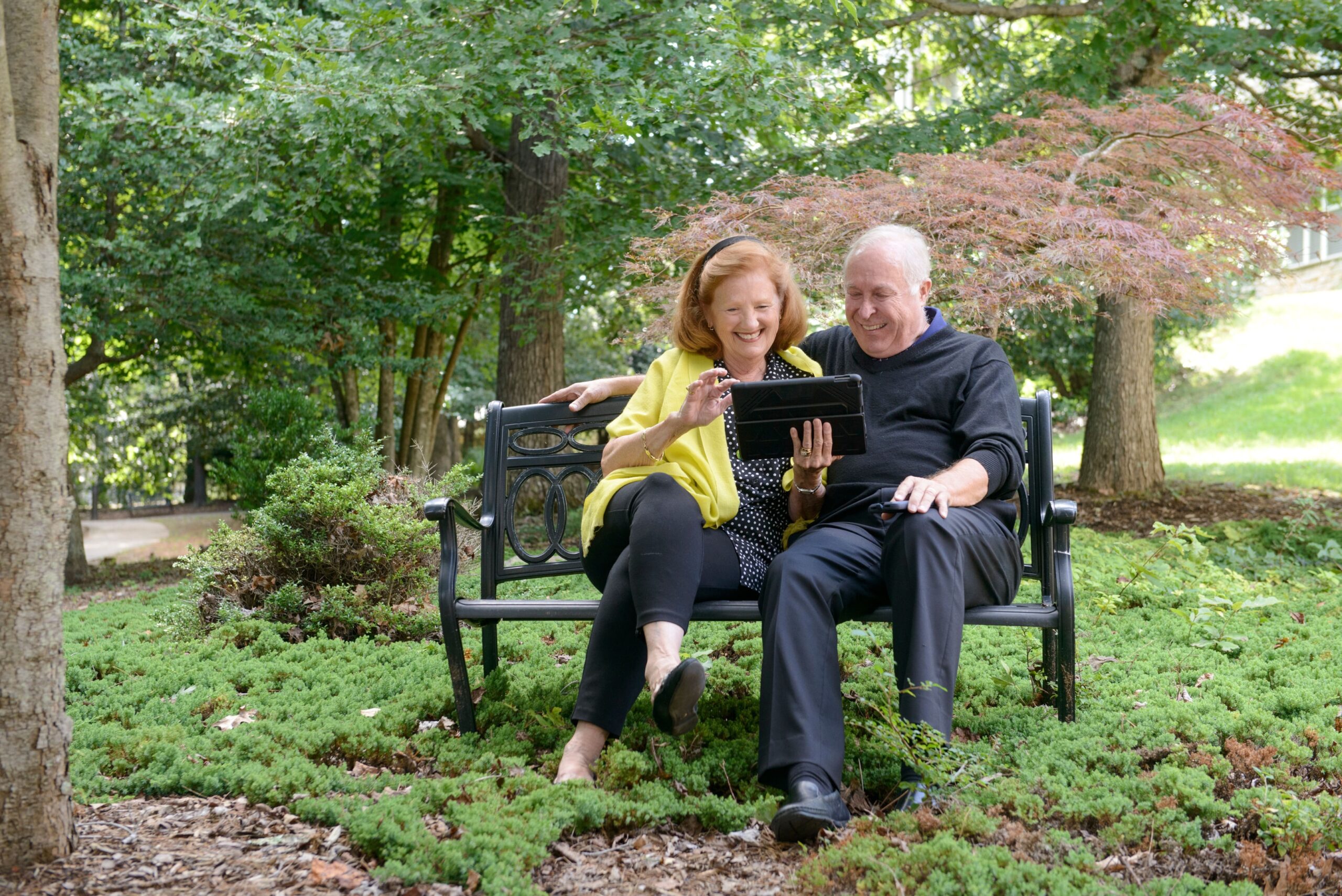 A man and woman sitting on a bench at Deerfield Episcopal Retirement community looking at a tablet
