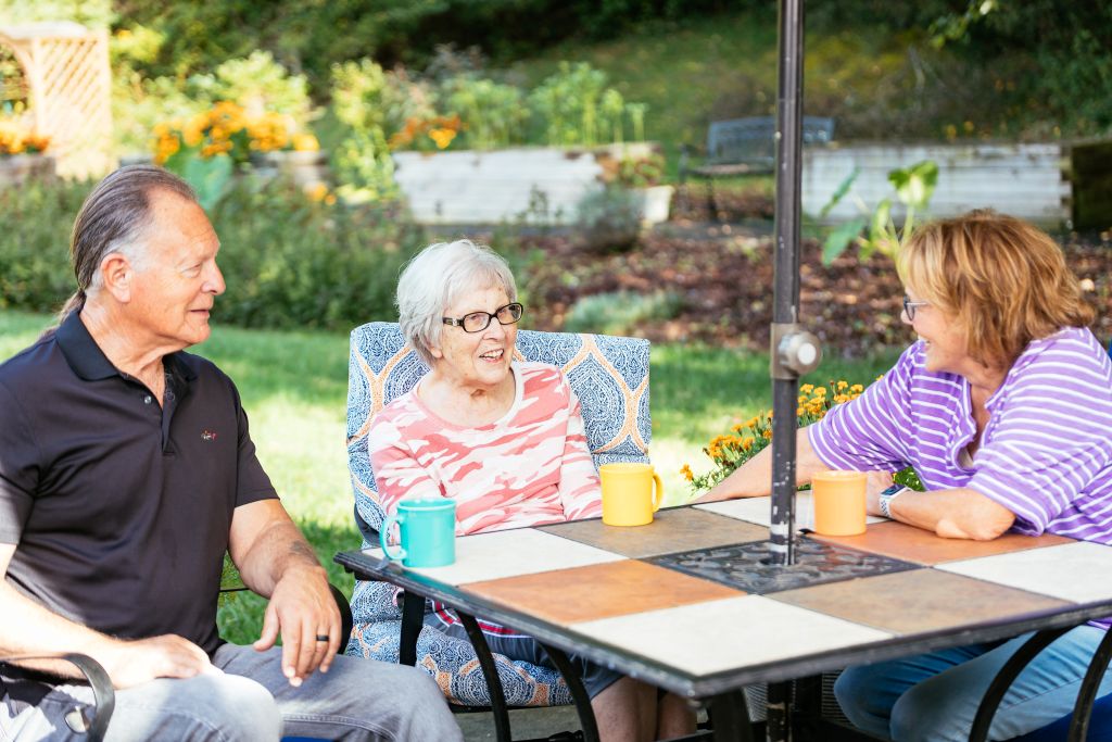 Three people having a drink at a patio table at Heather Glen at Ardenwoods